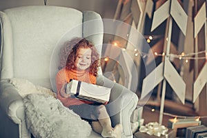 little girl with a Christmas gift sitting in a comfortable chair