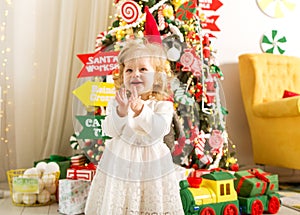 Little girl in christmas stands under a christmas tree in white