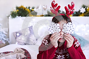 A little girl in a Christmas sweater plays with New Year`s snowflakes. Happy child in a festive light room. There is a