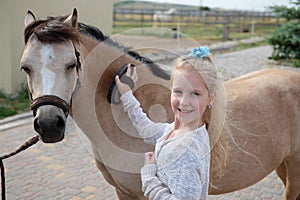 Little girl cleans and combs her pony and saddles him