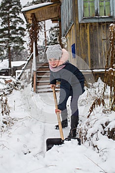 Little girl cleans snow to shovel near the country house.