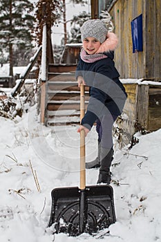 Little girl cleans snow to shovel near the country house.