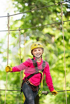 Little girl climbing in adventure activity park with helmet and safety equipment. Enjoy childhood years. Helmet and