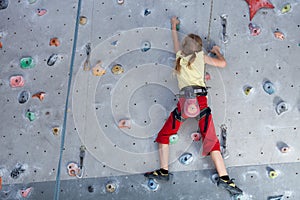 Little girl climbing a rock wall indoor.