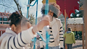 Little girl climbing rope ladder on playground close up. African mom looking kid