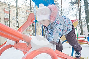 Little girl climbing on snowy playground seesaw