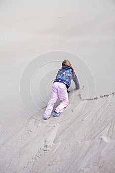 Little girl climbing up dune in the summer