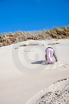 Little girl climbing up dune in the summer