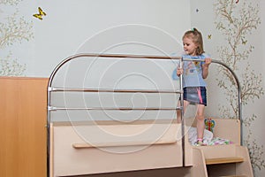 Little girl climbs on the bed holding the handrail