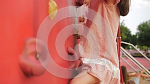 A little girl climbs a children's climbing wall on a playground in the park.