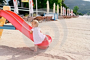 Little girl climbs a slide on a sandy beach