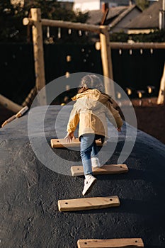 Little girl climbs up the hill on playground. Lot of enegry