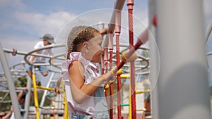 Little girl climbs up rope wall on playground