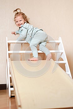 A little girl climbs a wooden slide in the gym. The child goes in for sports and develops