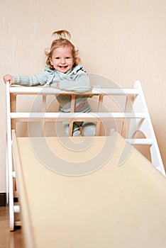 A little girl climbs a wooden slide in the gym. The child goes in for sports and develops