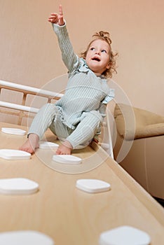 A little girl climbs a wooden slide in the gym. The child goes in for sports and develops