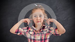 Little girl closed ears with fingers on grey background