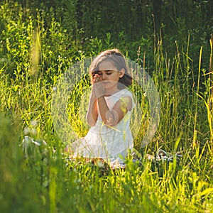 Little Girl closed her eyes, praying in a field during beautiful sunset. Hands folded in prayer concept for faith