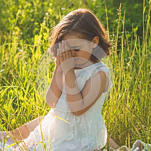 Little Girl closed her eyes, praying in a field during beautiful sunset. Hands folded in prayer concept for faith