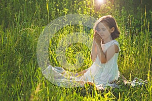 Little Girl closed her eyes, praying in a field during beautiful sunset. Hands folded in prayer concept for faith