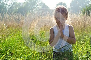 Little girl closed her eyes praying at sunset. Hands folded in prayer concept for faith, spirituality and religion. Hope, concept.