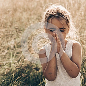 Little girl closed her eyes praying at sunset. Hands folded in prayer concept for faith, spirituality and religion. Hope, concept.