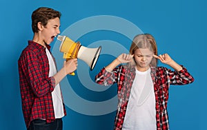 Little girl closing ears while her elder brother shouting to megaphone