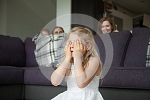 Little girl closing eyes playing hide and seek with family
