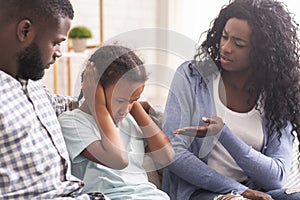 Little girl closing her ears not to listen parents scolding