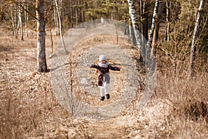 Little girl in a coat runs along a forest path