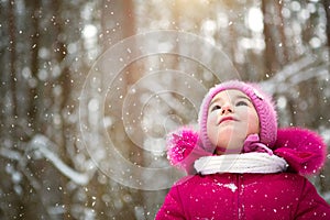 Little girl in the cold looks at the snow from the sky. Winter, walk the baby in the open air, snow. Warm clothing, knitted hat,