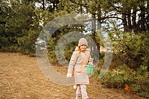 A little girl collects cones in a plastic baby bucket