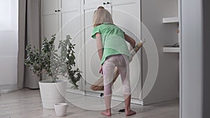 A little girl collects the earth from the laminate. Cute baby removes garbage from the floor of the house