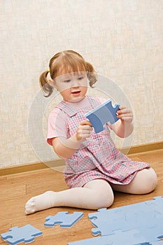 Little girl collects puzzles in a room