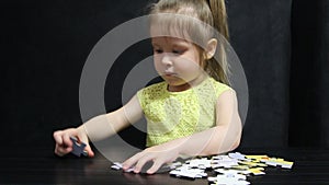 Little girl collects puzzles at the table on a dark gray background