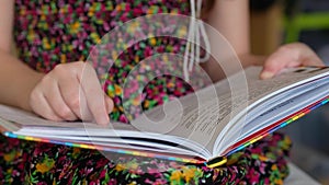 Little girl in a colorful dress is reading a book. Child learns to read.