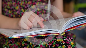 Little girl in a colorful dress is reading a book. Child learns to read.