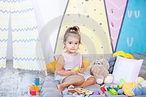 Little girl in colorful wigwam with toys. child plays with colorful toy blocks. Developing and creative toys and games for young c