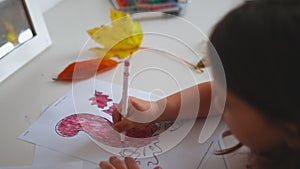 Little girl coloring a squirrel image on a paper sheet with a red marker