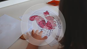 Little girl coloring a squirrel image on a paper sheet with a red marker