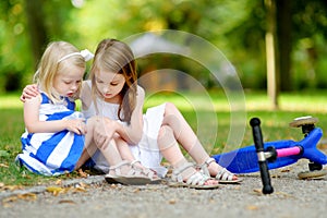 Little girl comforting her sister after she fell while riding her scooter