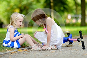 Little girl comforting her sister after she fell while riding her scooter