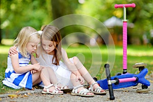 Little girl comforting her sister after she fell while riding her scooter