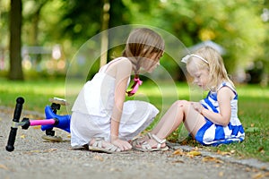 Little girl comforting her sister after she fell while riding her scooter