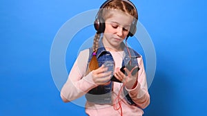 A little girl connects the headphones to the phone and enjoys the music