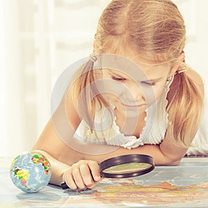 Little girl considering a world map with a magnifying glass