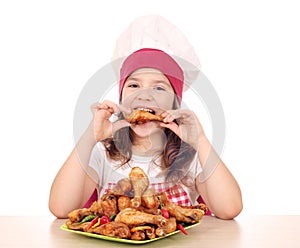 Little girl cook eating chicken drumstick photo