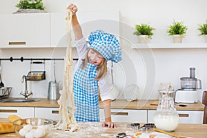 Little girl in a cook plays with a dough on a table and smiles