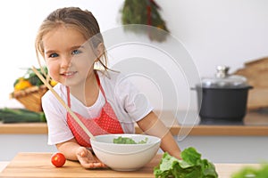 Little girl cooking in the kitchen. Kid slicing and mixing tomatoes and greenery. Concept of healthy meal or tasty