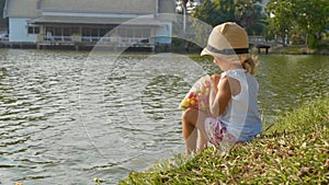 Little girl in country style hat feeding fishes in a park lake